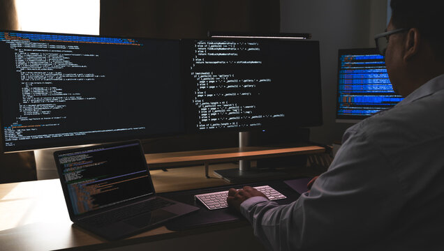 programmer working at a multi monitor computer setup with code on screens in a dark workspace, illustrating software development, coding, debugging, and technical workflow in office context.