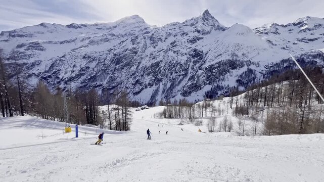 Group of skiers descending a groomed slope in the Alps with majestic snow-capped mountains in the background. Winter sports activity on a sunny day at a ski resort with breathtaking mountain panorama.