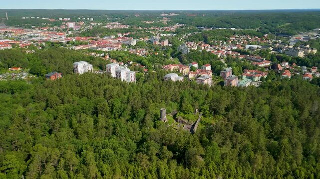 Drone parallax shot descends over historic stone castle ruins of Tureborg Slott with Uddevalla city skyline in background