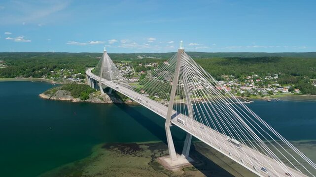 Aerial pull back reveals massive highway Uddevalla bridge spanning Sunninge Sound and Byfjorden with traffic flowing over blue water