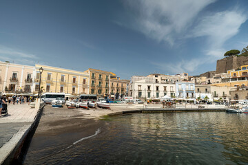 Obraz premium Mondello beach waterfront in Palermo, Sicily with colorful historic buildings, fishing boats, and Mediterranean architecture under blue sky.