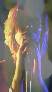 Female singer gripping microphone stand and leaning into mic, performing music with bracelet, bokeh