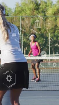 Two adult female tennis players playing on hard court wearing visors and hitting ball with racquets