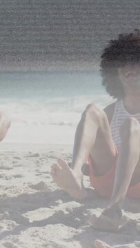 Vertical video: Camera panning pair on beach shifting, patting sand, scanline overlay for travel