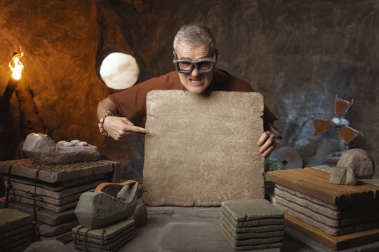Caveman in his office showing a stone tablet with blank space
