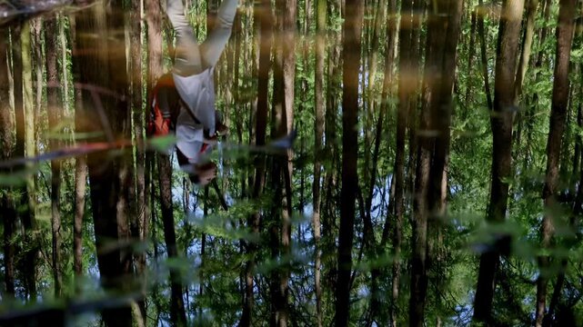 Young girl trekker hiking on wood trail pathway with backpack to admire jungle stream exploration, woman wipes sweat from forehead with hand show tired expression, moment of calm water reflection