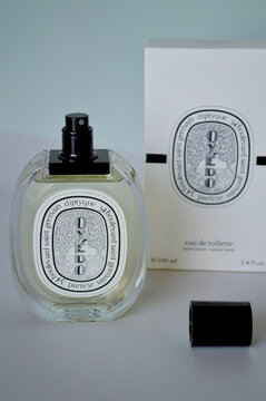 Elegant glass bottle of Diptyque Oyedo Eau de Toilette fragrance with white packaging box and black cap displayed on a minimalist studio background with soft lighting.