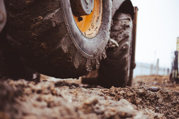 A close-up of an excavator tire lifted off the muddy ground due to a heavy load on the bucket shows the power and heaviness of construction machinery at work. © Rystemys