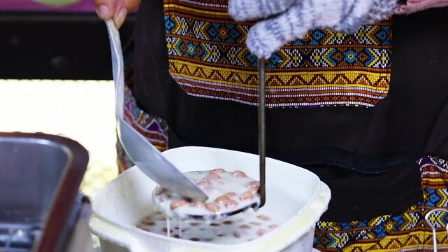 A close-up shot of a person preparing crispy lotus blossom cookies or dok jok, a popular thai dessert, by dipping the mold in batter and deep frying it in hot oil for a delicious snack.