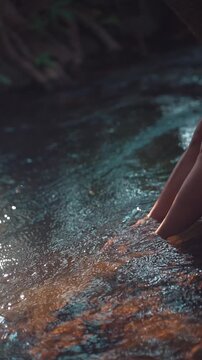 Woman barefoot legs standing in clear forest stream water, persom feet in tropical river with flowing water and natural relaxation scene, 4k vertical video