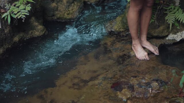 Woman barefoot legs standing in clear forest stream water, persom feet in tropical river with flowing water and natural relaxation scene 4k