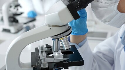 Scientific professional wearing blue protective gear examining microscope lens, performing detailed...
