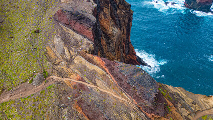 Dramatic aerial view of Ponta de Sao Lourenco's vibrant geological cliffs and winding coastal trail, with the Atlantic Ocean crashing below. © Viktor