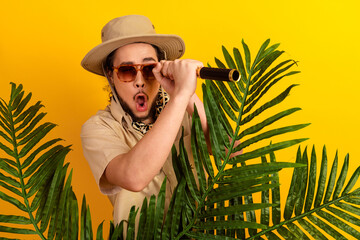Naklejka premium Adventurous traveler with safari hat and mic among tropical leaves under a yellow backdrop