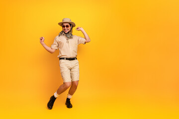 Obraz premium Young man in safari outfit dances happily against a bright yellow backdrop wearing hat scarf and sunglass