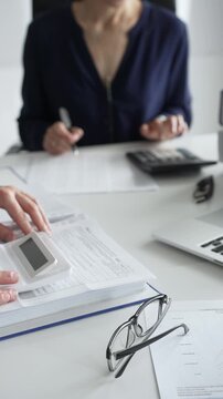 Close up of male financial analysts examining documents with female colleague, using calculator at workplace in office. Audit and taxes concept