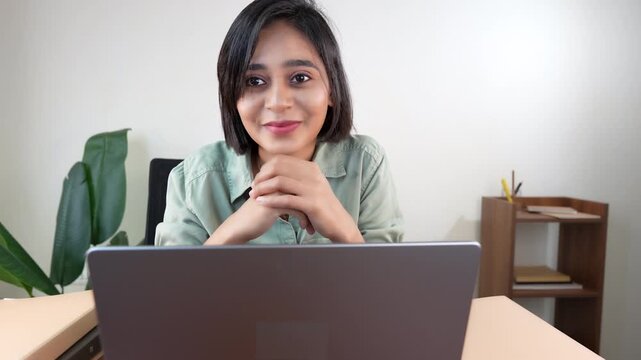 Close up of happy smiling successful young working business woman sits on chair at workplace desk look at camera with positive face expression.