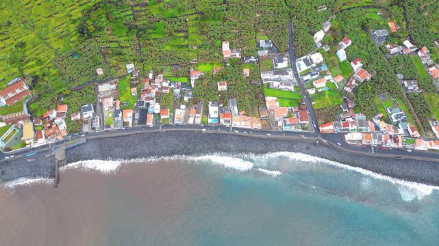 Aerial view of a vibrant Paul do Mar village on Madeira, where lush green terraced fields meet the deep blue Atlantic and a charming row of houses.