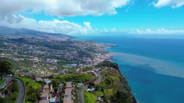 Funchal, Madeira's capital, sprawls across volcanic hillsides to the Atlantic. Lush landscapes meet the vibrant blue ocean under a partly cloudy sky. Cabo Girao