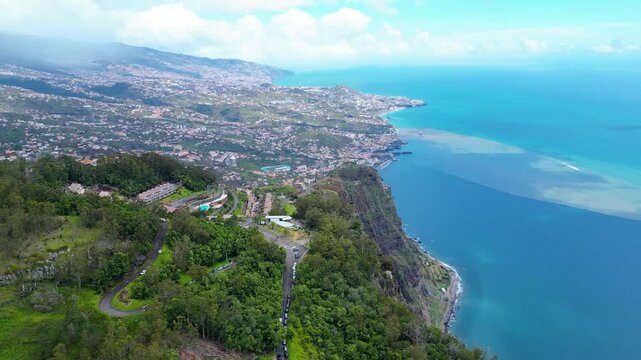 Funchal, Madeira's capital, sprawls across volcanic hillsides to the Atlantic. Lush landscapes meet the vibrant blue ocean under a partly cloudy sky. Cabo Girao