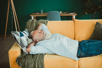 Calm senior man rests on bright orange couch at home in cozy living room scene ideal for lifestyle and real estate visuals © deagreez