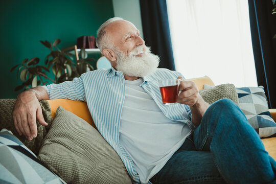 Senior man relaxes at home enjoying tea on the couch in a cozy living room scene in a bright modern interior