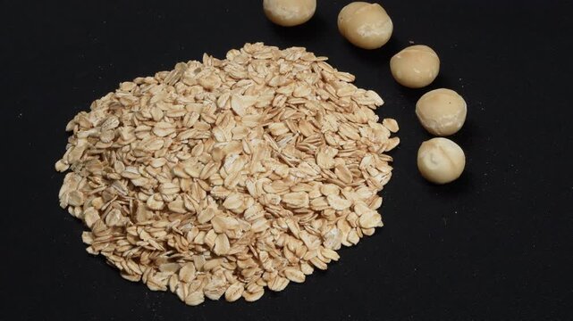 Macro of organic rolled oats and macadamia nuts rotating on black background.