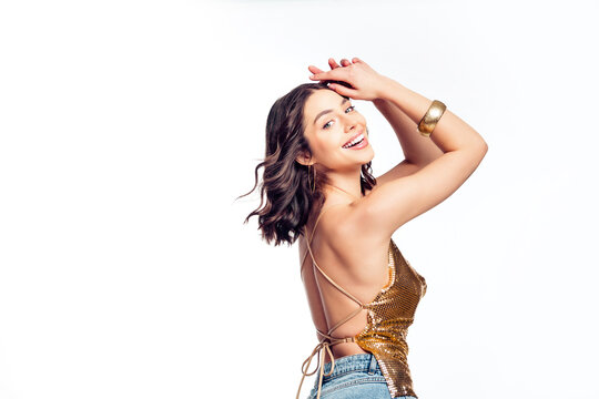 Smiling young woman in a gold sequin backless top posing confidently for a fashion portrait, joyful and glamorous party style expression