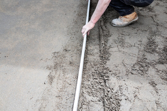 Worker leveling concrete with screed for slab foundation
