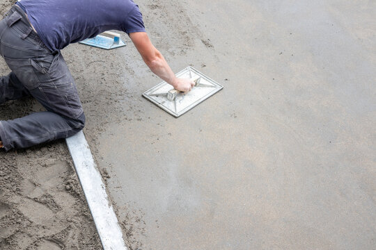 Worker smoothing fresh concrete surface with trowel