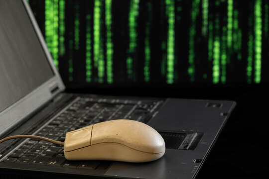 a vintage, worn-out serial mouse, from the 1990s, placed on top of a laptop keyboard with a matrix background