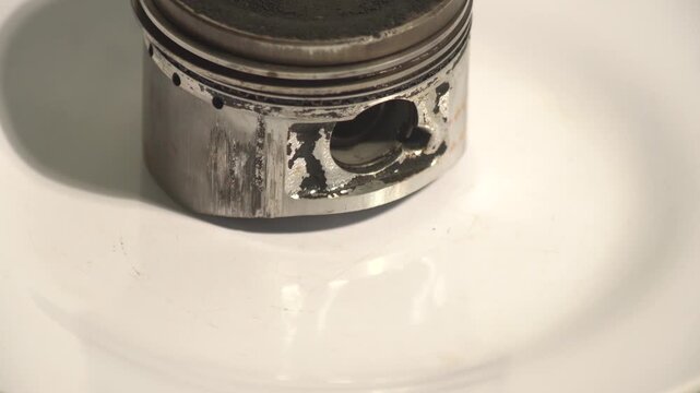 Damaged and scratched engine piston with heavy carbon deposits rotating on a clean white background. Perfect for internal combustion engine failure, mechanical breakdown, automotive repair, and vehicl