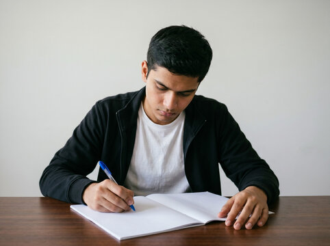 indian male student writing exam at desk with focused expression representing competitive exam preparation study and academic success concept