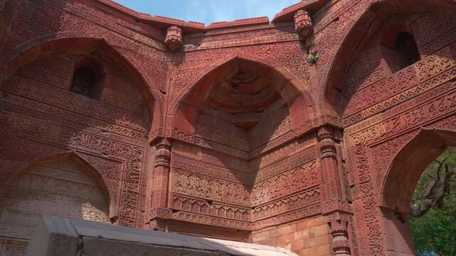 A static low-angle shot showing the ornate Indo-Islamic architectural details of the arches and walls within the Qutb Minar complex, featuring geometric patterns and inscriptions in New Delhi.
