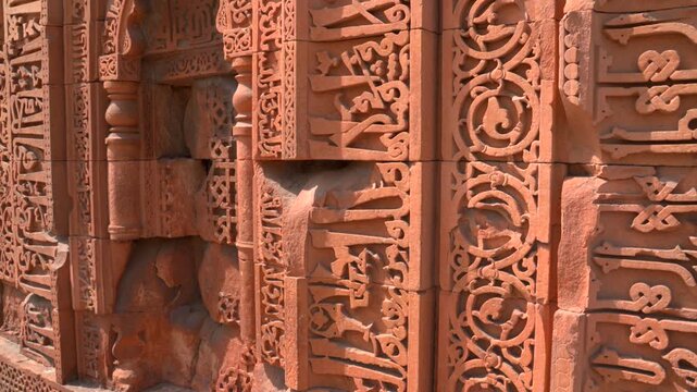 A static close-up shot of the intricately carved red sandstone facade of the Qutb Minar, highlighting the ancient Kufic script and delicate geometric and floral motifs.
