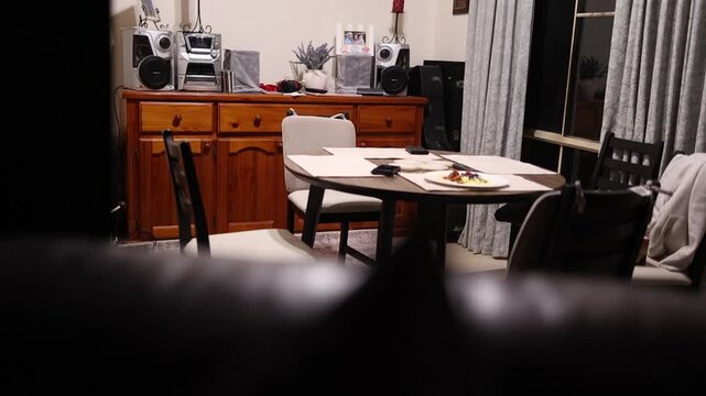 Warm and inviting dining room features wooden furniture and modern stereo. Evening lighting creates a relaxed atmosphere, while the composition highlights homely aesthetics.