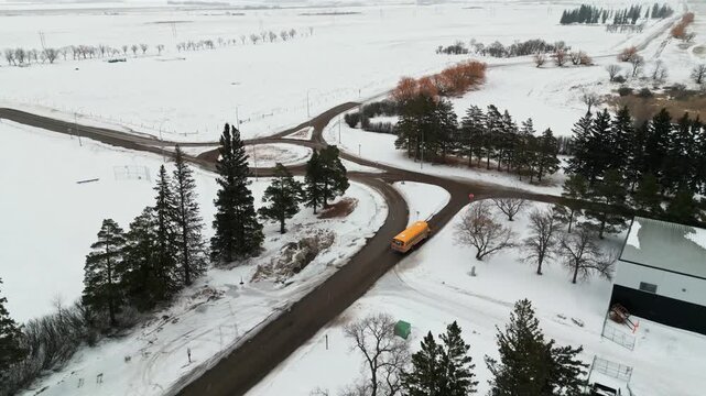 Aerial drone shot of a yellow school bus driving in small town Saskatchewan winding roads.