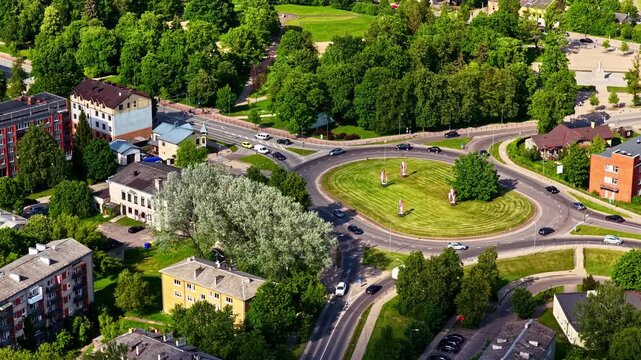 A cinematic drone zoom capturing the flow of cars navigating a green city traffic circle.