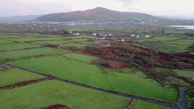 Drone shot flying toward the ancient Cahergal Stone Fort, the massive circular structure amidst the lush green patchwork fields and distant mountains of rural Kerry, Ireland