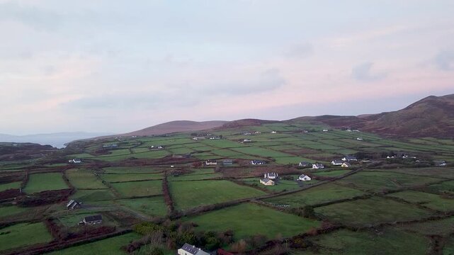 Drone establishing shot of green patchwork fields, traditional white farmhouses, and rolling hills near the village of Eyeries in rural Cork, Ireland