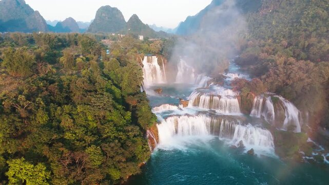 Cinematic drone shot flying away from the tiered Ban Gioc Waterfall. Reveals the expansive limestone mountain landscape and lush forest of Cao Bang province in Northern Vietnam.