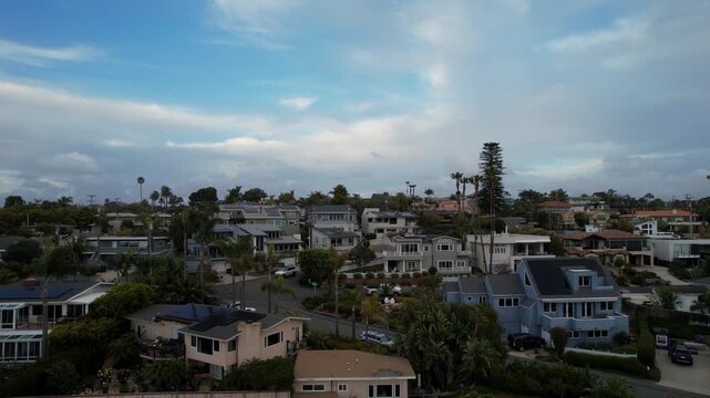 Drone pulling back across a street and out over the ocean at 9AM with camera facing toward coastal homes in Encinitas California.