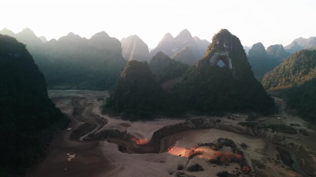 Cinematic drone flight forward toward the famous God's Eye Mountain (Angel Eye) in Cao Bang, Vietnam. Misty limestone karst peaks and a winding valley floor are bathed in soft morning sunlight.