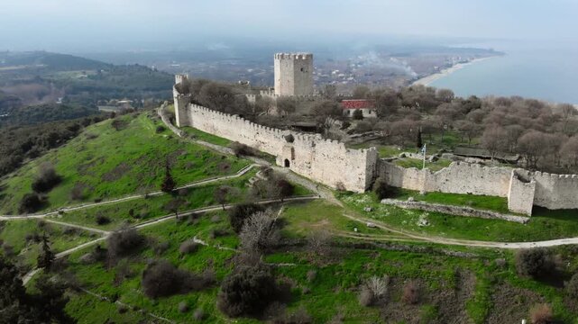 An ancient fortress with a prominent tower and extensive stone walls, set against a coastal backdrop. Ideal for historical documentaries or travel features.