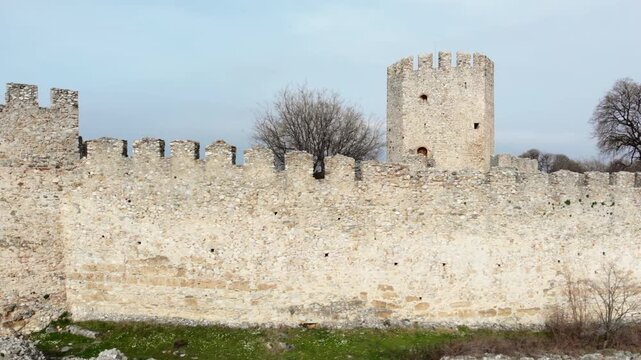 A sturdy fortress with a central tower and bare trees stands under an overcast sky. Ideal for historical documentaries or educational content.