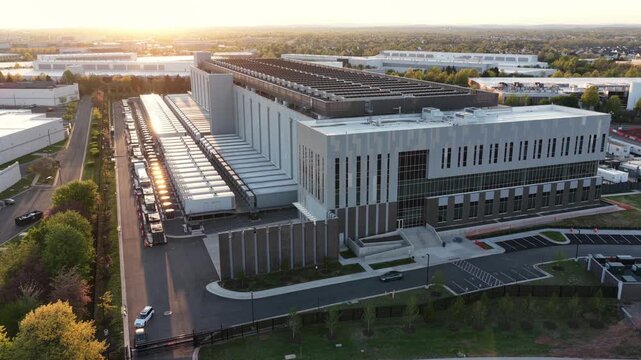 Modern data center in Ashburn, Virginia at sunset with an electric car driving nearby, sustainable infrastructure, cloud computing and advanced AI technology in USA. Aerial backwards wide shot.