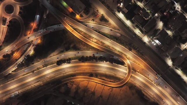 Elevated drone perspective capturing the flow of vehicles on an illuminated urban highway network, showing the complexity of city infrastructure and transportation routes after dark