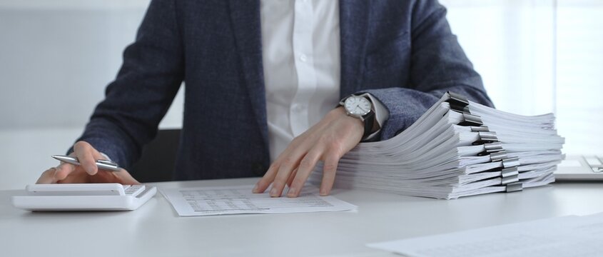 Business professional sorting a large stack of financial reports and tax forms with binder clips on a busy office desk. Audit and taxes