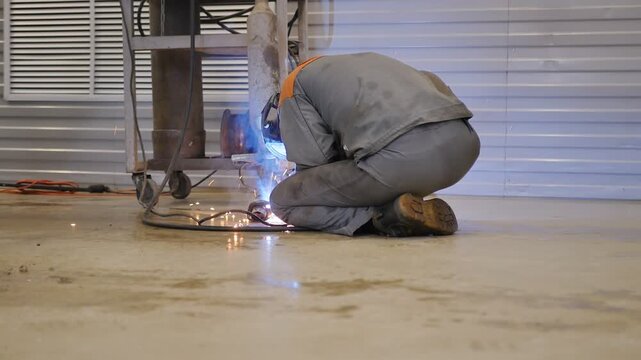 Medium shot welder sitting on floor welds metal at resonator of car muffler clamped in vise for vertical welding. Semi automatic welding strong and reliable. Auto welder at work.
