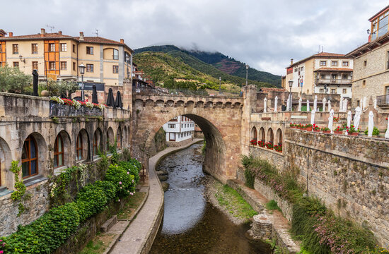 Vista del hist&oacute;rico puente de piedra de San Cayetano sobre el r&iacute;o Deva, rodeado de arquitectura tradicional y flores en el centro de Potes, Cantabria, Espa&ntilde;a